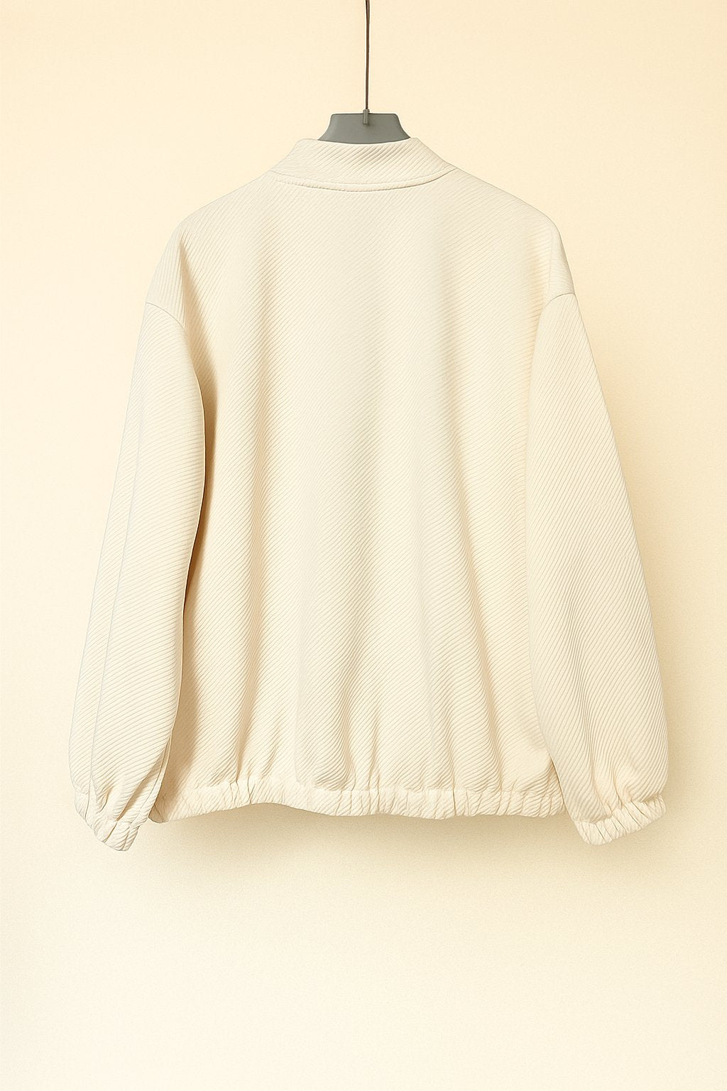 Hanger flatlay, back view of the apricot textured bomber jacket showing the rib-knit collar, drop-shoulder seam and gathered elastic hem.