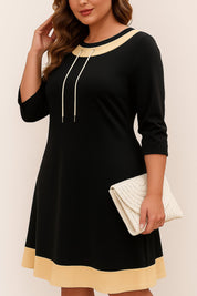 Relaxed front three-quarter view of the black A-line dress with beige contrast trim, drawstring neckline and three-quarter sleeves.