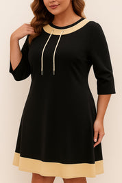 Front three-quarter view of the black A-line dress showing the beige contrast trim, drawstring neckline and three-quarter sleeves.
