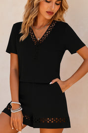 Front three-quarter view of the black eyelet-trim V-neck top and shorts set; buttoned split-placket and hem eyelet bands visible