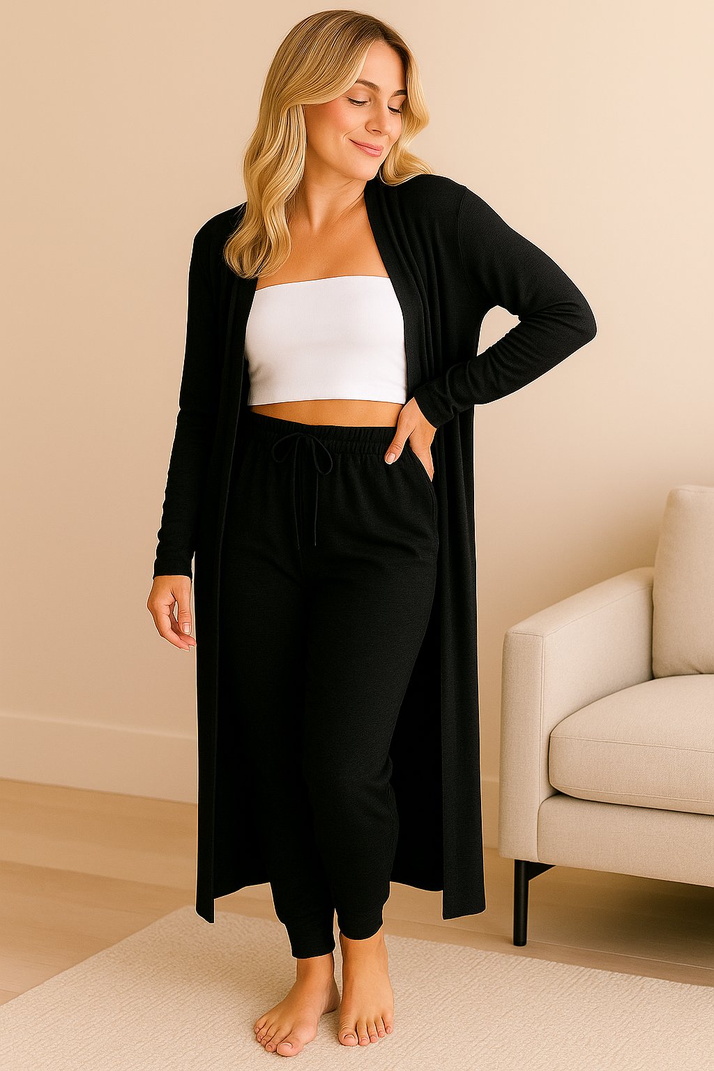 Woman in elegant black loungewear set with long cardigan, jogger pants, and white bandeau top in cozy home interior