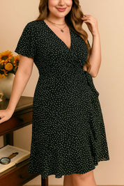 Plus-size black polka-dot wrap mini dress with V-neck and side tie bow, relaxed drape — front three-quarter view