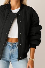 Front detail view of the black quilted bomber jacket showing the rib-knit collar, snap-button placket over the zipper and wave quilting.
