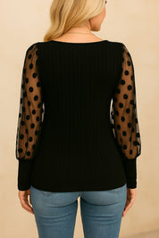 Black blouse showing polka-dot mesh sleeve fabric and rib-knit body texture — front detail close-up view