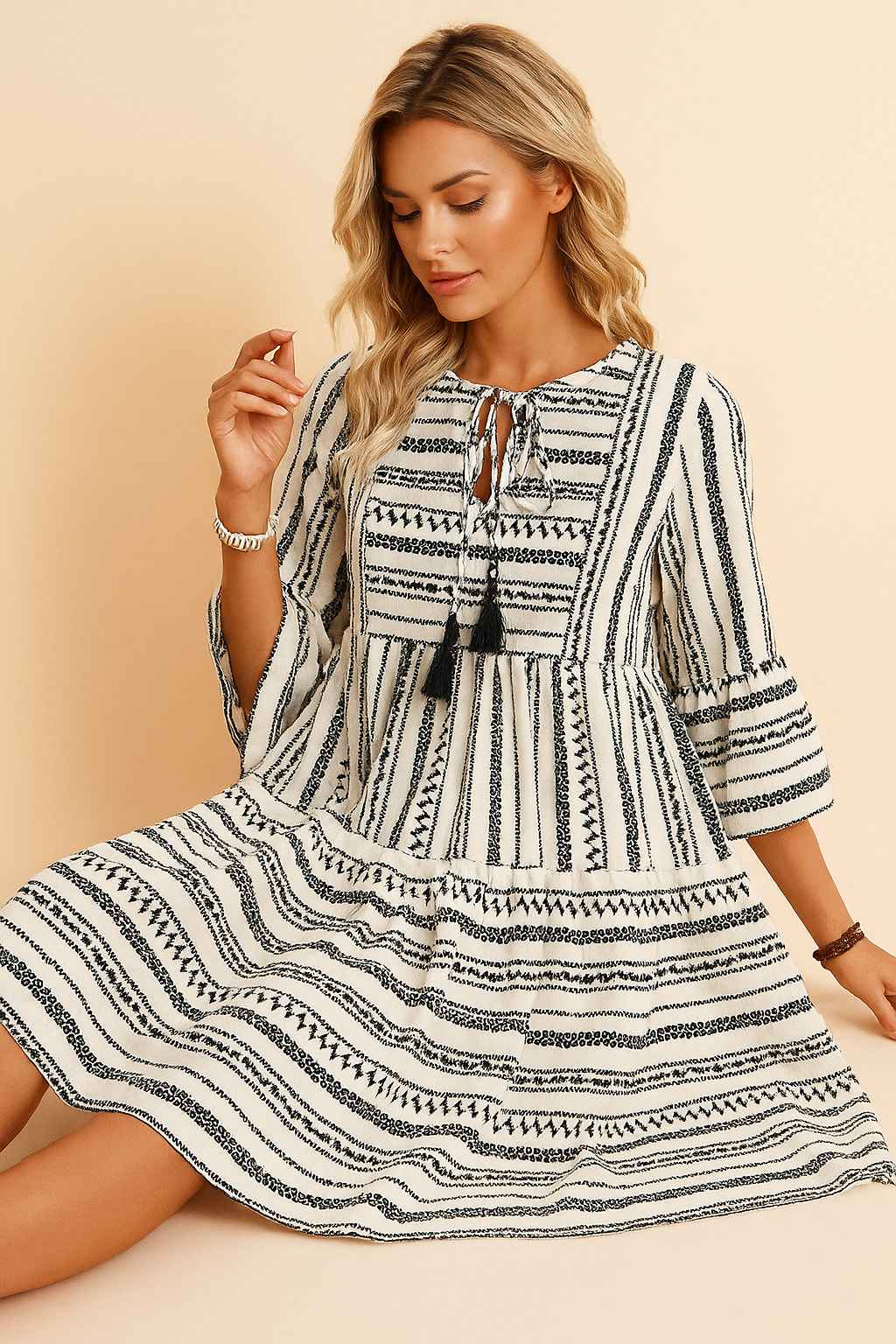 Black-and-white boho-print tie-neck mini dress with tassel ties, three-quarter sleeves and tiered skirt — seated front view