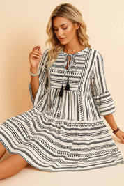 Black-and-white boho-print tie-neck mini dress with tassel ties, three-quarter sleeves and tiered skirt — seated front view