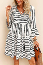 Black-and-white boho-print tie-neck mini dress with tassel ties, three-quarter sleeves and tiered skirt — seated front view