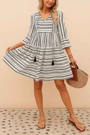 Black-and-white boho-print tie-neck mini dress with tiered skirt and tassel accents — front view, hem sway