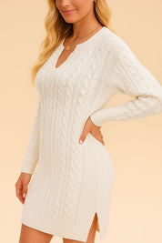 Close side view of a women’s cable-knit sweater dress featuring a V-notch neckline, long sleeves, ribbed cuffs and hem, and a subtle side slit that eases movement and flatters the shape.