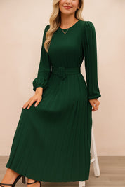 Dark-green belted pleated long-sleeve midi dress with crew neckline and fitted waist — seated front view