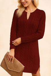 Woman wearing a burgundy cable knit dress holding a beige clutch against a beige background