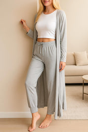 Relaxed woman in a light gray three-piece loungewear set with joggers, long cardigan, and white crop top in a modern living room