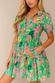 Floral button-down babydoll dress in green multi with shirt collar, side pockets, puff sleeves and tiered skirt — front view, pocket entry.