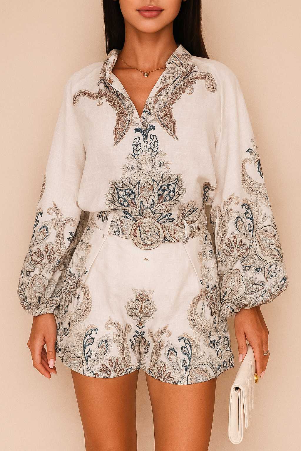 Front view of a women’s grey paisley long-sleeve blouse with split V neckline and billowed sleeves paired with belted shorts featuring slant pockets