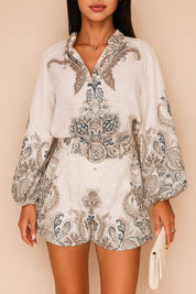 Front view of a women’s grey paisley long-sleeve blouse with split V neckline and billowed sleeves paired with belted shorts featuring slant pockets