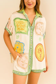 Front view of an ivory-multi printed short-sleeve button-up shirt with matching shorts; shirt collar, relaxed fit and side pockets with green trim.