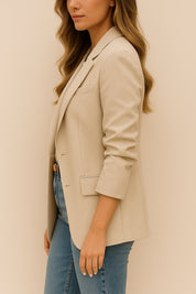“Left side view of the khaki longline blazer showing the notched lapel, single-breasted front and flap pocket at the hip.