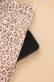 Close-up of leopard print pajama pants showing functional side pocket with smartphone, soft stretchy fabric