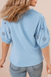 “Back view of the light blue puff-sleeve blouse with floral eyelet sleeves and a curved back hem