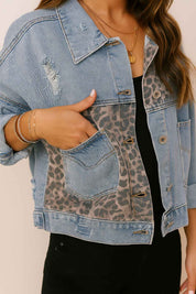 Front detail view showing the slant pocket opening on the light-wash denim jacket with leopard-panel insert and light distressing