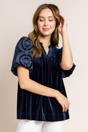 Navy velvet blouse with embroidered puff sleeves and soft notched neckline, easy relaxed silhouette — seated front view.