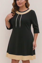Short lookbook video of a black A-line dress with beige contrast trim, drawstring neckline and three-quarter sleeves, shown in studio lighting.