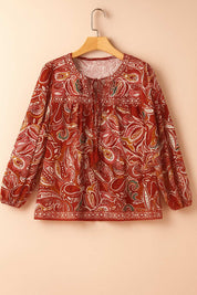 Hanger flatlay, front view of the red-multi paisley blouse highlighting the tassel-tie neckline, gathered yoke and border print at the hem.