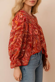 Left three-quarter view of the red-multi paisley tassel-tie blouse showing the gathered neckline, billowy sleeve and elastic cuff