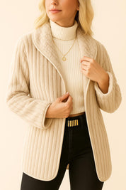 Woman wearing a beige ribbed sweater over a white turtleneck with black pants on a beige background