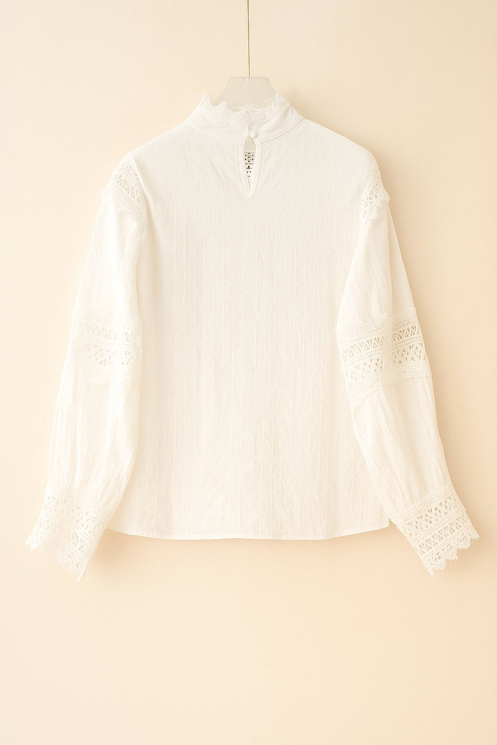 Hanger flatlay, back view of the white high-neck blouse with a small keyhole button at the neck and fine vertical texture; lace sleeve bands visible