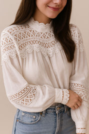 Left three-quarter view of the white lace-yoke high-neck blouse showing the sleeve lace bands and straight rounded hem