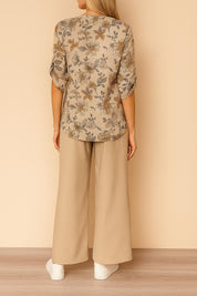Centered back view of the apricot floral blouse with roll-tab sleeves paired with beige wide-leg pants; relaxed silhouette