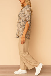 Left side view of the apricot floral blouse with roll-tab sleeves and the beige wide-leg pants; soft, easy movement.