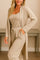 Woman in beige three-piece loungewear set featuring long cardigan, tank top, and drawstring jogger pants in neutral-toned room
