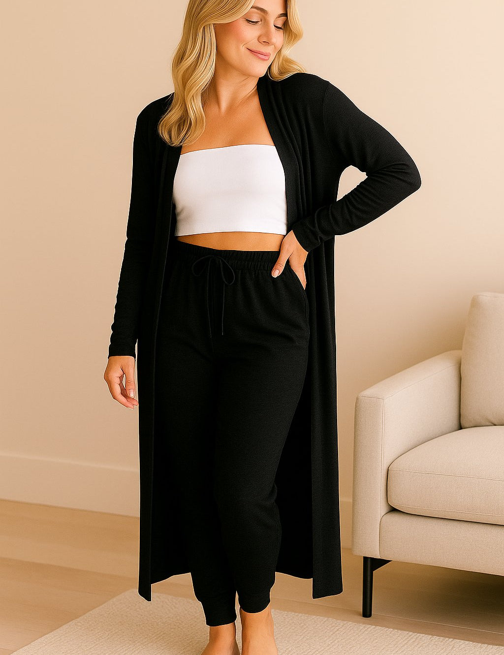 Woman in elegant black loungewear set with long cardigan, jogger pants, and white bandeau top in cozy home interior