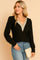 Front three-quarter view of a women’s black ribbed knit V-neck blouse with beige crochet trim at the neckline and long sleeves; straight hem