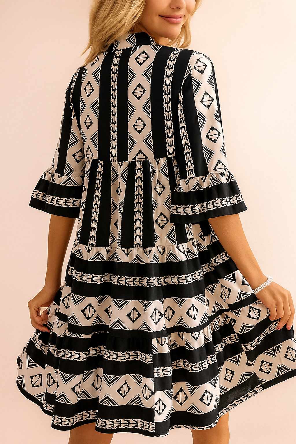 Black-and-white boho geometric tiered mini dress with flared half sleeves and clean straight mini hem — back view.