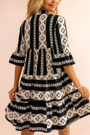 Black-and-white boho geometric tiered mini dress with flared half sleeves and clean straight mini hem — back view.