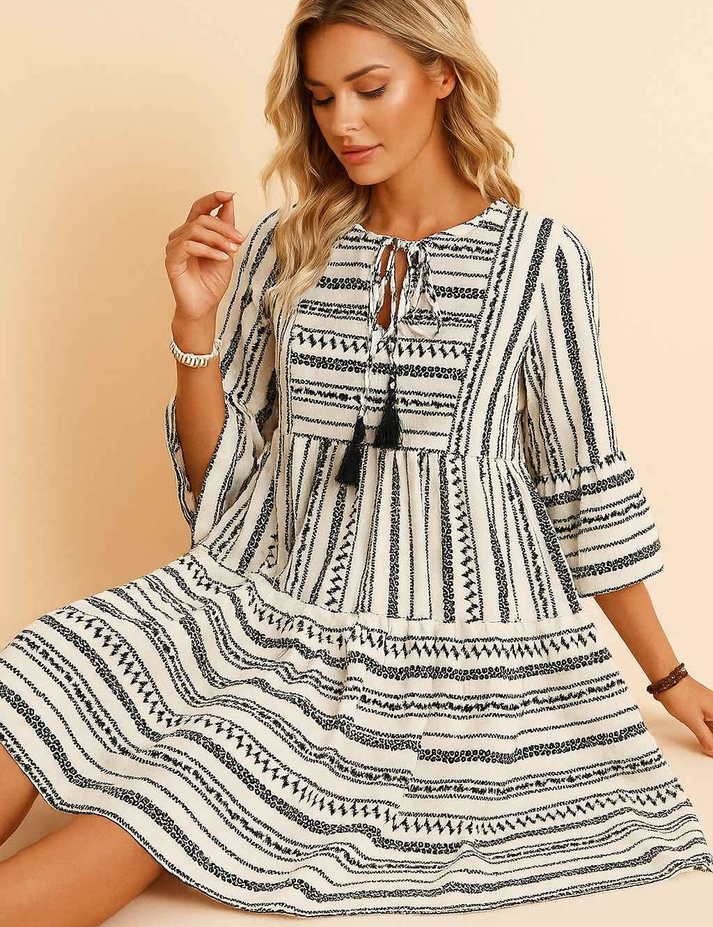 Black-and-white boho-print tie-neck mini dress with tassel ties, three-quarter sleeves and tiered skirt — seated front view