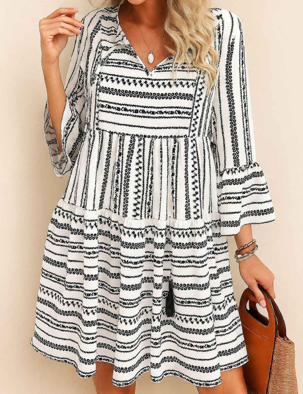 Black-and-white boho-print tie-neck mini dress with tassel ties, three-quarter sleeves and tiered skirt — seated front view
