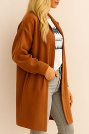 Left side view of the caramel textured button-down collared longline coat showing the drop-shoulder sleeve and slant welt pocket opening.