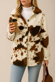 Front view of the ivory and brown cow-print fuzzy button-up jacket with open placket; shirt collar and patch pocket detail visible.