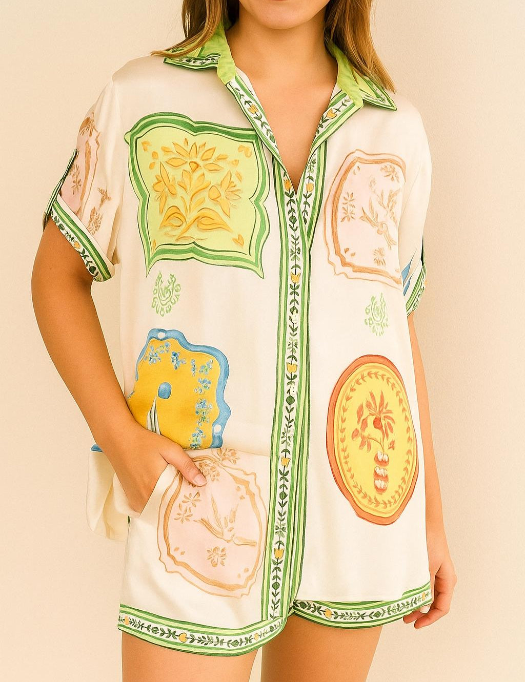 Front view of an ivory-multi printed short-sleeve button-up shirt with matching shorts; shirt collar, relaxed fit and side pockets with green trim.