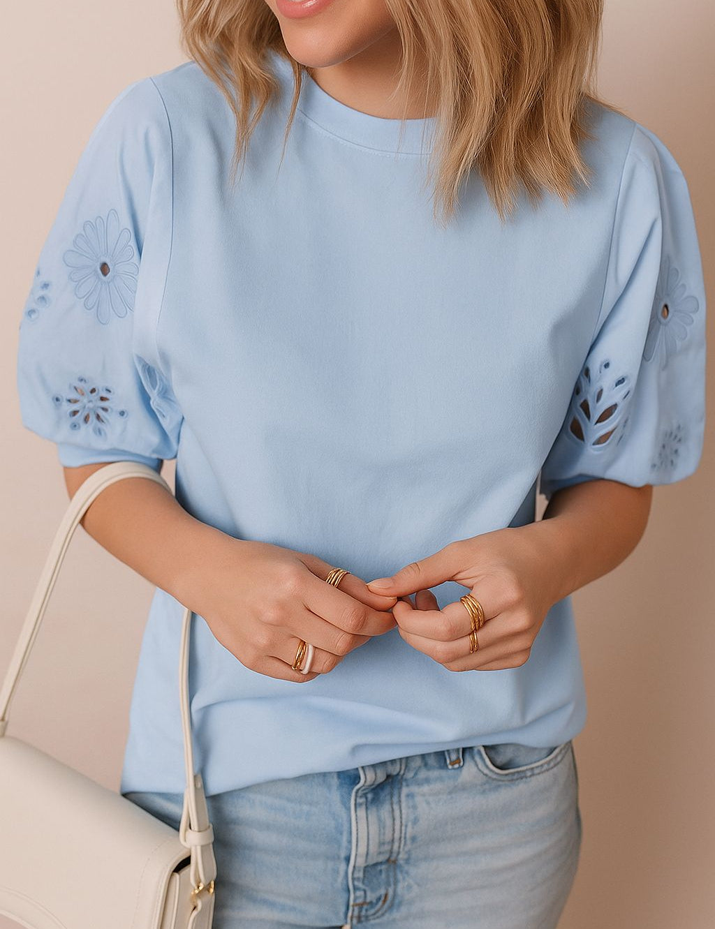Close front detail view of a light blue puff-sleeve blouse with floral eyelet embroidery on the sleeves and a clean crew neckline