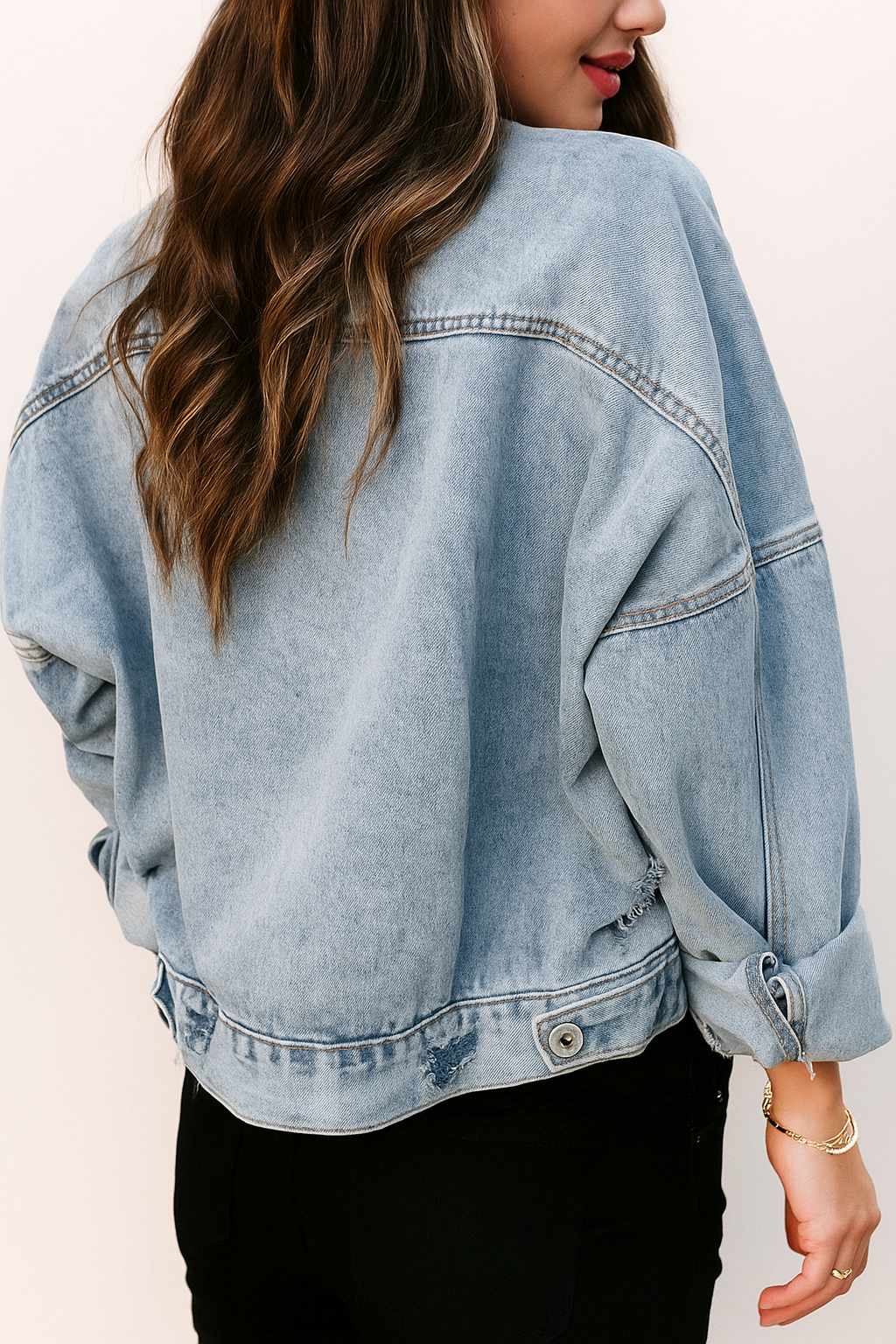 Back view of the light-wash drop-shoulder denim jacket with wave fading, rear yoke and light distressed marks along the hem.