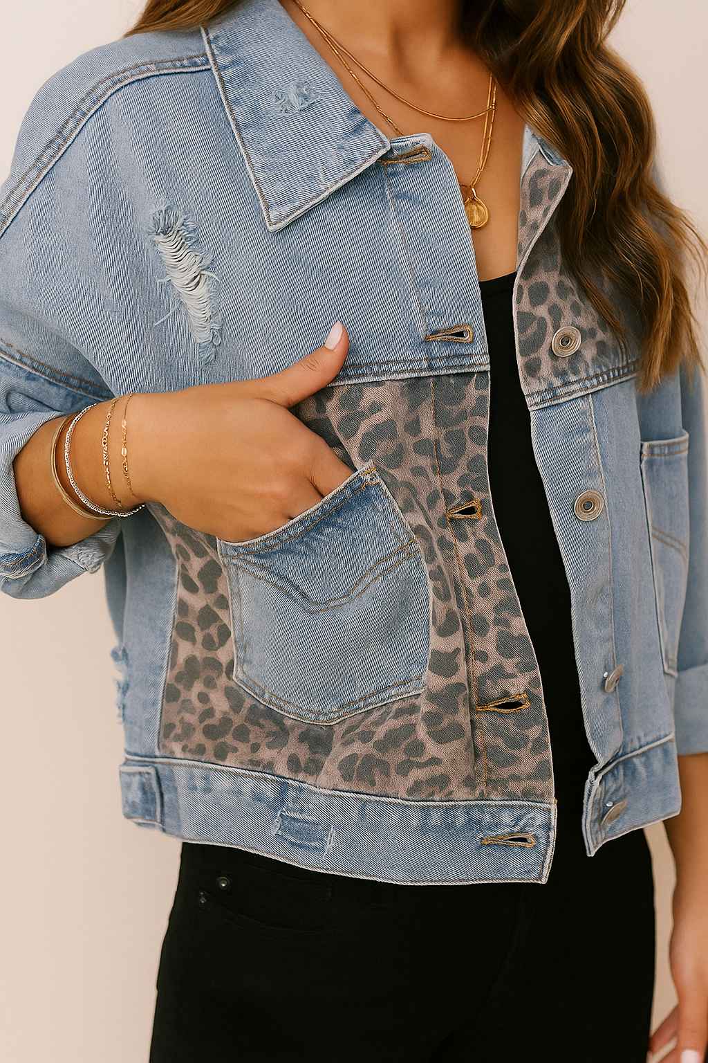 Front detail view showing the slant pocket opening on the light-wash denim jacket with leopard-panel insert and light distressing