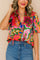 Front detail view of a women’s rose-multi tropical print tie-neck short-sleeve blouse with a soft V split and lightly ruffled collar