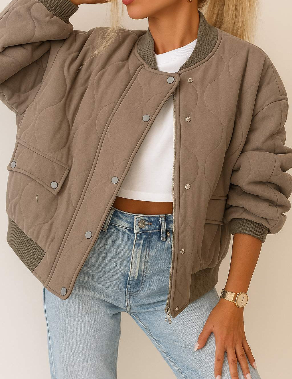 Front detail view of a taupe quilted bomber jacket with rib-knit collar and cuffs, zip front with snap-button placket, and snap-flap patch pockets.