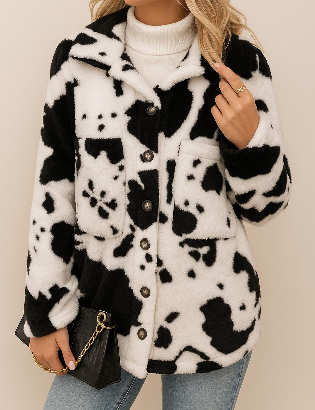 Front view of a women’s white and black cow-print fuzzy button-up jacket with a shirt collar, long sleeves, patch pockets and a rounded hem.