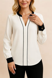 Centered front view of the white notched V-neck blouse featuring black contrast piping and button cuffs; rounded hem.